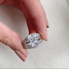 a woman's hand holding an engagement ring in her left hand, with the center stone surrounded by diamonds