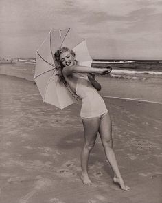 a woman in a bathing suit holding an umbrella on the beach