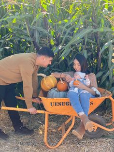 a man and woman pushing a wheelbarrow full of pumpkins