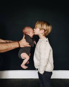 a man is giving a baby a kiss on the cheek as he stands in front of a black wall