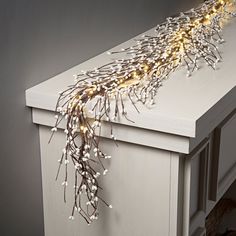 a white dresser with some lights on it's top and branches hanging from the drawer