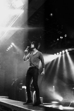 a man standing on top of a stage holding a microphone in front of him and lights behind him