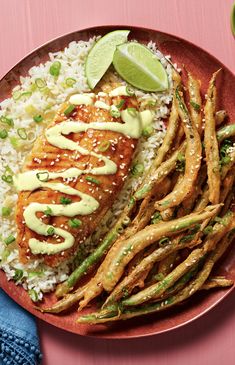 a red plate topped with fish and asparagus covered in mayonnaise next to rice