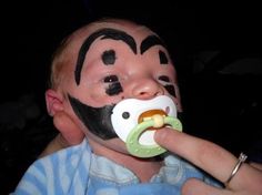 a young boy with face painted like a monkey eating something out of a green cup