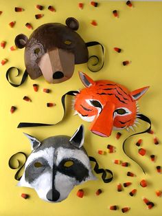 two paper masks are on a yellow surface with candy streamers around them and one has a fox, the other is a raccoon