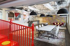 an office with red railings and white tables in the center, surrounded by black pendant lights