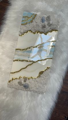 a piece of glass with gold and white designs on it sitting on a fur rug