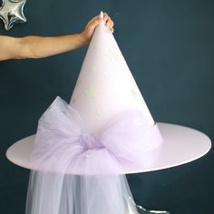 a person holding a pink party hat on top of a white cake plate with purple tulle