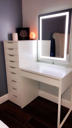 a white desk with a lighted mirror and drawers in front of it on top of a hard wood floor