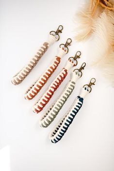 four different colored beads are hanging from hooks on a white surface next to feathers and feather clippings