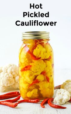 a jar filled with cauliflower sitting on top of a table next to red peppers