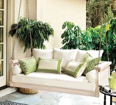 a white porch swing with green pillows and plants on the back wall, in front of an open patio door