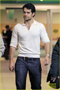 a man in white shirt and jeans walking through an airport terminal with his hand on his hip