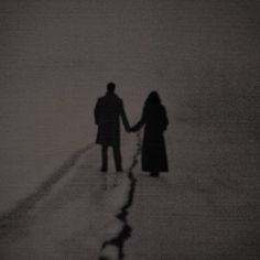 two people holding hands while walking on the beach in the snow at sunset or dawn