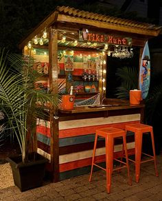 an outdoor bar with two stools in front of it and lights on the outside