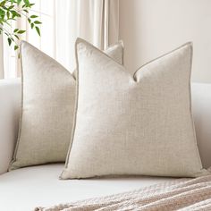 two pillows sitting on top of a white couch next to a potted green plant