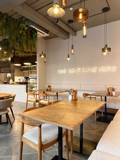 an empty restaurant with wooden tables and white booths, hanging lights and plants on the wall