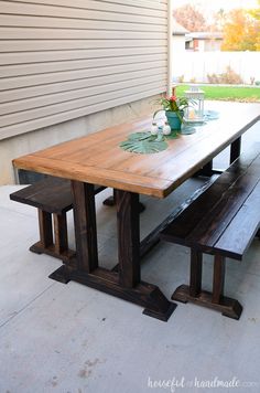 a wooden table with benches in front of it on a patio next to a house