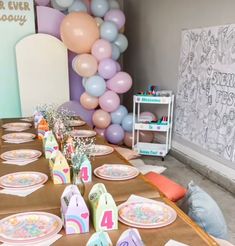 a table set up for a birthday party with balloons in the back ground and decorations on the wall