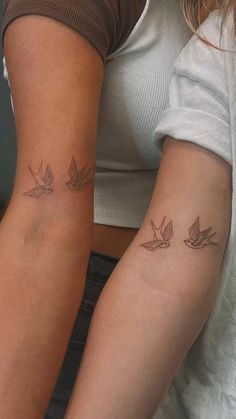 two women with matching tattoos on their arms, one has a bird and the other has a dove