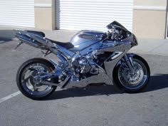 a shiny silver motorcycle parked in a parking lot next to a building with shutters