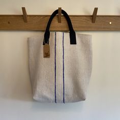 a white and blue bag hanging from a wooden hook on a wall with a black handle