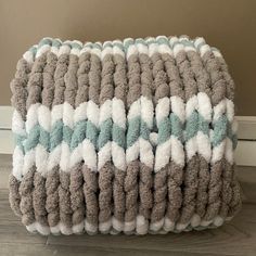 a gray and white blanket sitting on top of a wooden floor next to a wall