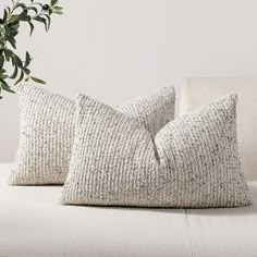 two pillows sitting on top of a white couch next to a potted green plant