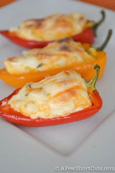 three red peppers with cheese on them sitting on a white plate, ready to be eaten