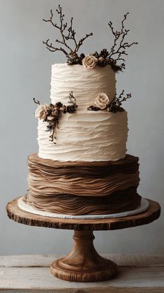 a three tiered cake with white frosting and dried flowers on top, sitting on a wooden stand