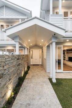 a white house with an attached walkway and stone wall next to the front door is lit up by recessed lights