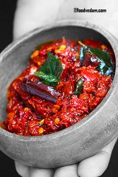 a person holding a small bowl filled with red sauce and green leafy garnish