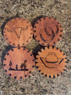 three wooden coasters with designs on them sitting on a granite countertop in front of a stone wall