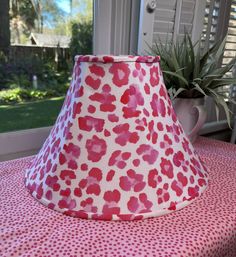 a pink and red lamp shade sitting on top of a table next to a potted plant