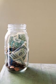 a glass jar filled with money sitting on top of a wooden table next to a wall