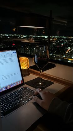 a person sitting at a table with a laptop and wine glass in front of them