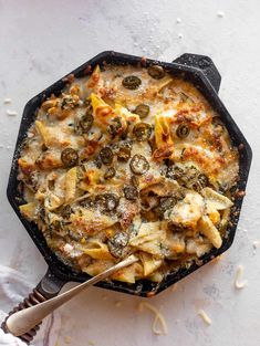 a skillet filled with pasta and mushrooms on top of a table next to a fork