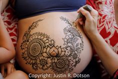 a pregnant belly with henna tattoos on it's side and someone writing something in her hand