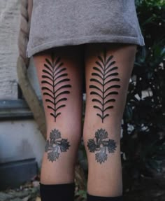 two women with tattoos on their legs are standing in front of some bushes and trees