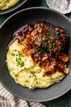 meat and mashed potatoes in a bowl with sauce on the side, ready to be eaten