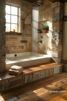 a bath tub sitting next to a window in a room with wood floors and stone walls