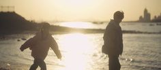 two people walking on the beach at sunset