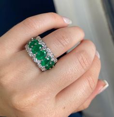 a woman's hand holding an emerald and diamond ring