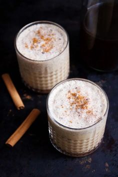 two glasses filled with drink sitting on top of a black table next to cinnamon sticks