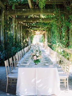 a long table is set with white linens and place settings for an outdoor dinner