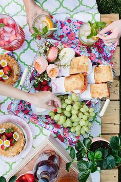 an overhead view of food and wine on a picnic table with people holding glasses of wine