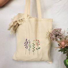 a tote bag with flowers on it next to a potted plant and vase