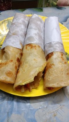 three burritos on a yellow plate sitting on a table