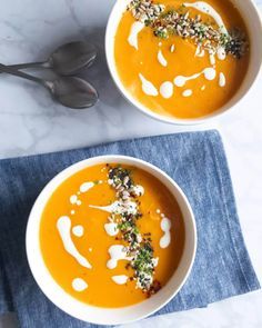 two bowls filled with carrot soup on top of a blue napkin next to silver spoons