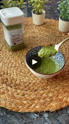 someone is dipping pesto into a bowl with a spoon on the table next to some potted plants